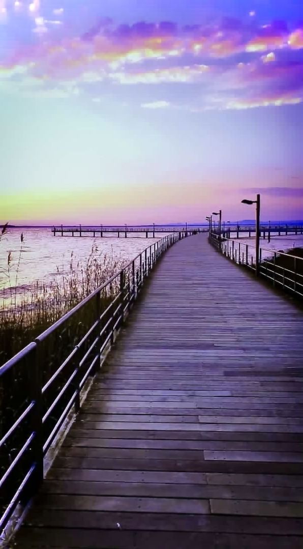 sky, water, pier, walkway, sea, boardwalk, horizon, cloud, scenics - nature, nature, sunset, wood, beauty in nature, tranquility, dusk, tranquil scene, the way forward, evening, beach, railing, footpath, architecture, land, jetty, horizon over water, no people, built structure, coast, diminishing perspective, reflection, shore, outdoors, bridge, travel destinations, idyllic, ocean, landscape, purple, non-urban scene, footbridge, sunlight, holiday, environment, travel, seascape