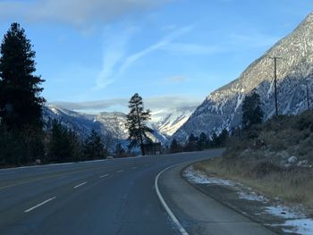 Road by trees against sky during winter