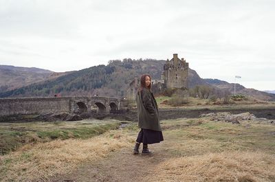 Rear view of woman standing on grassy field against sky
