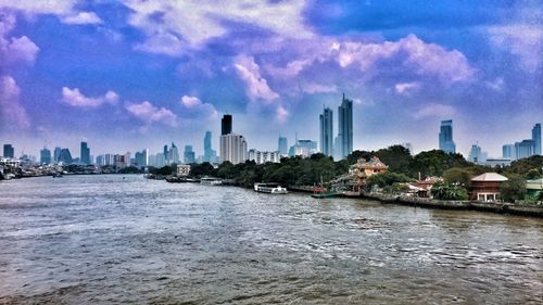 Buildings by river against sky in city