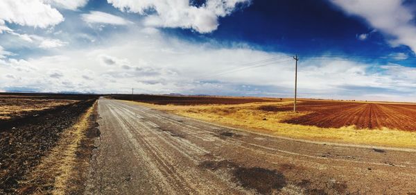 Dirt road amidst field against sky