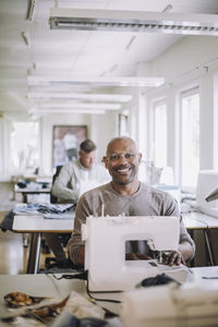 Portrait of smiling fashion designer by sewing machine at workshop