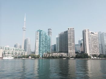 Modern buildings by river against clear sky in city