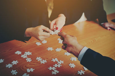 Cropped image of friends playing jigsaw puzzle at table