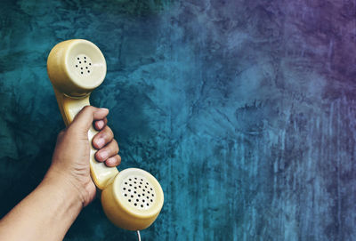 Cropped hand of person holding telephone receiver against wall