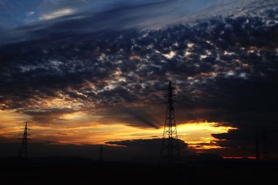 Silhouette of electricity pylon against cloudy sky