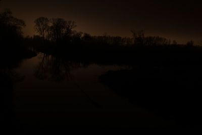 Reflection of silhouette trees in lake against sky during sunset