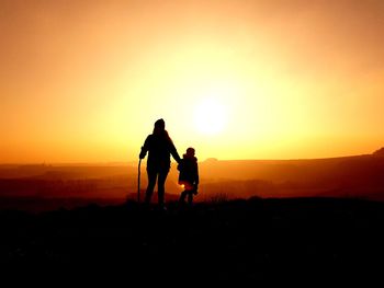 Silhouette men on landscape against sky during sunset