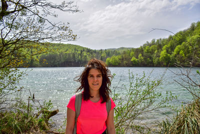 Portrait of beautiful woman standing by lake against sky