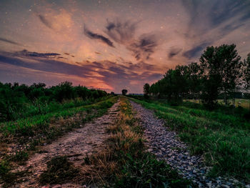 Road amidst field against sky during sunset