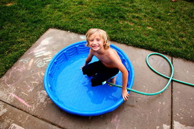 Portrait of smiling shirtless boy in wading pool in back yard