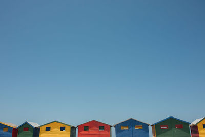 Low angle view of beach huts against clear blue sky