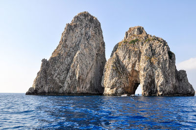 Rock formation in sea against clear blue sky