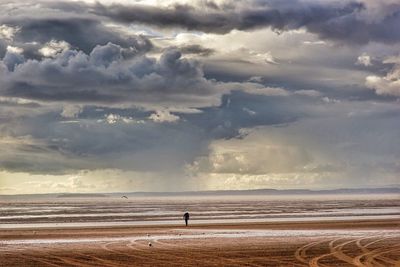 Man on shore at beach against cloudy sky