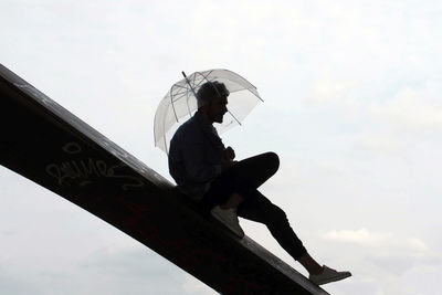 Low angle view of man sitting against sky