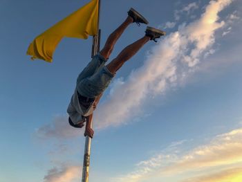 Low angle view of man balancing on pole against sky during sunset