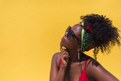 Contemplating young woman wearing sunglasses against yellow background