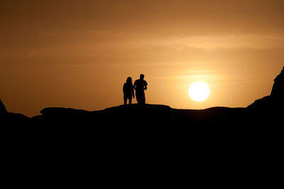 Silhouette of people standing on mountain at sunset