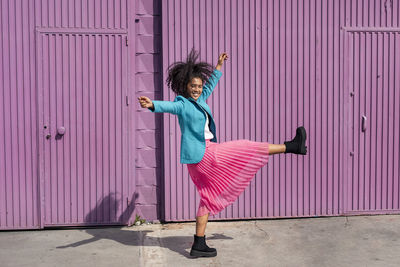 Woman with arms outstretched standing against pink wall