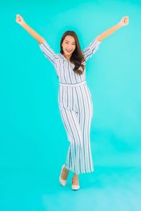 Young woman with arms raised against blue background