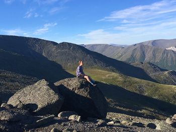 Man sitting on rock by mountains against sky