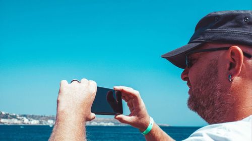 Close-up of man photographing by sea against sky