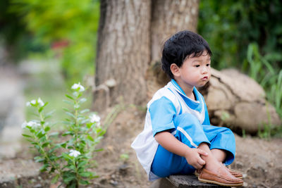 Cute boy sitting on plant outdoors