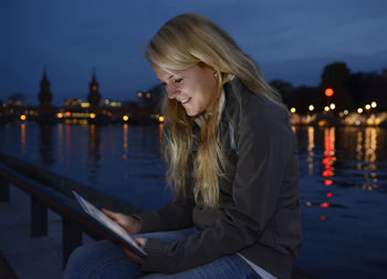 Smiling woman using digital tablet while sitting in illuminated city at night