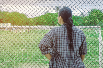 Rear view of woman standing by chainlink fence