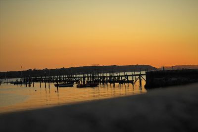 Silhouette pier on sea against orange sky