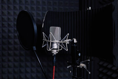 Contemporary metal microphone with wire placed on background of soundproof foam with pyramid shaped pattern in dark music recording studio