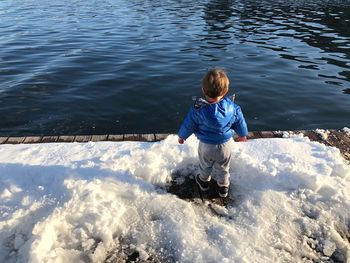 Rear view of boy standing on snow covered pier by lake