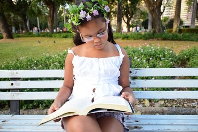 Girl reading book while sitting on bench at park