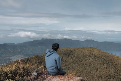 Rear view of man sitting on mountain against sky.