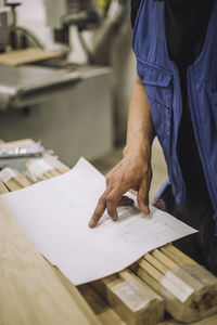 Midsection of mature blue-collar worker reading blueprint in warehouse