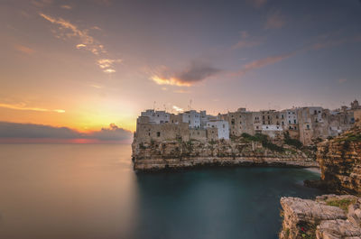 Scenic view of sea by buildings against sky during sunset