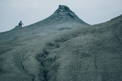 Low angle view of man sitting on mountain against sky