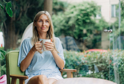 A happy smiling woman sits in a coffee shop against the backdrop of a huge window.