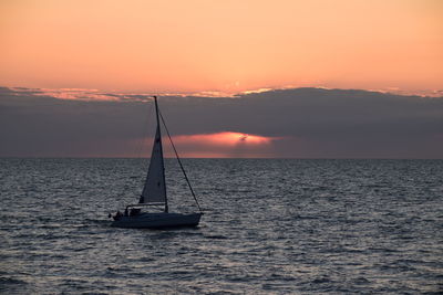 Silhouette sailboat in sea against sky during sunset
