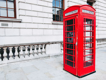 Red telephone booth on sidewalk in city