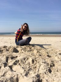 Woman sitting at beach against sky