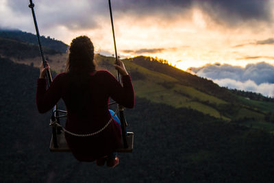 Rear view of woman on swing at sunset