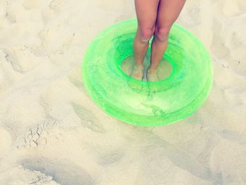 Low section of woman standing amidst green inflatable ring at sandy beach