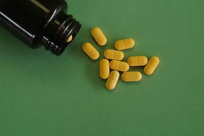 Close-up of pills spilling from bottle against green background