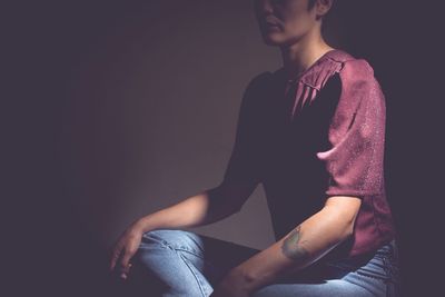 Midsection of young woman sitting against wall