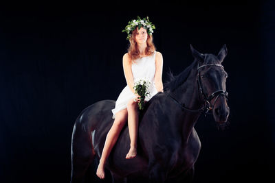 Young woman sitting on horse against black background