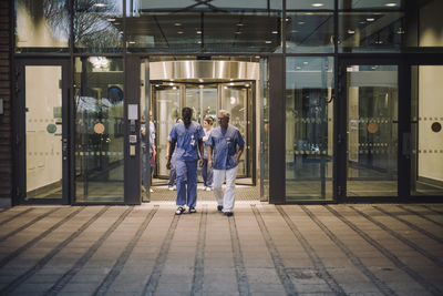 Multiracial male doctors in scrubs leaving hospital at night