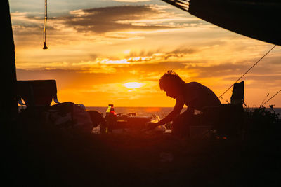 Silhouette people sitting by sea against sky during sunset