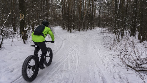 Rear view of man cycling on snow covered land