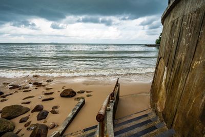 Shipwreck at beach against cloudy sky